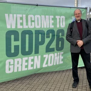 Dan Button stands next to a sign reading Welcome to COP26 Green Zone