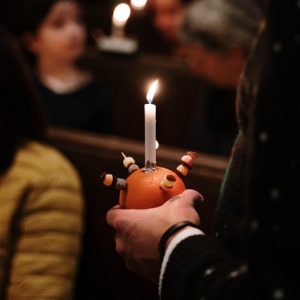 A Christingle orange in a darkened church with people holding candles in the background
