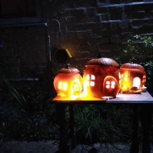 Three pumpkins carved to look like little houses, sitting on the table, with a candle burning inside each of them illuminating the windows.