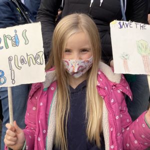 A little girl holding two banners saying There is no planet B and Save the planet