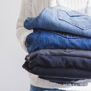 A person holds a pile of neatly folded jeans