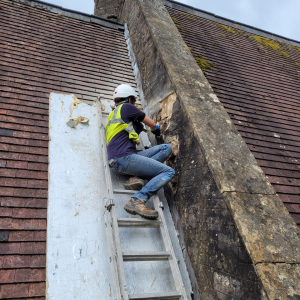 A person sitting at the top of a ladder making repairs to masonry