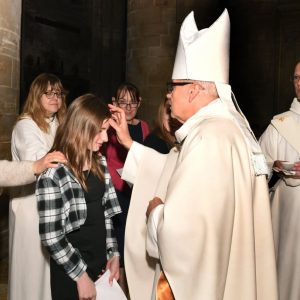 Bishop Robert marks the sign of the cross on a young woman's forehead while people pray for her