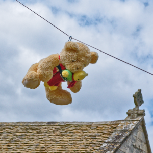 A teddy on a zip wire with another teddy in a sling on his front. A glimpse of an ornate cross on a weathered church roof is just visible in the background